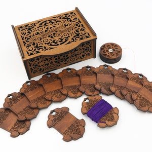 May include: A wooden craft organiser set with a decorative box, spools, and tags. The box and tags have intricate cut-out designs. The tags are arranged in an arc, with a spool of purple thread. The box has the text "my beloved Joanna".