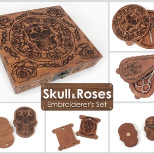 May include: Wooden embroidery set featuring a skull and roses design. The set includes a box, a needle case, and two thread bobbins. The box has a hinged lid and a latch. The needle case has a hinged lid and a small compartment for needles. The thread bobbins are shaped like skulls and have a small hole for threading.