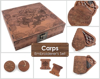 May include: A wooden box with a carved design of koi fish and a lotus flower. The box is open and shows a set of embroidery tools, including scissors, a needle threader, and a spool of thread. The box is labelled "Carps Embroiderer's Set".