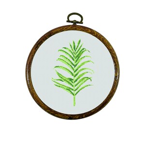 Op de afbeelding: Een groen palmblad kruissteekpatroon in een bruine houten borduurring.