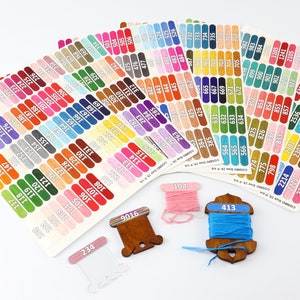 May include: A collection of DMC embroidery floss color cards with corresponding thread wound on wooden bobbins. The cards are labeled with DMC floss numbers. The bobbins are labeled with the numbers 104, 413, and 9016.