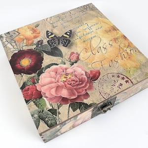 May include: A vintage-style wooden box with a floral design featuring pink, red, and yellow roses, green leaves, and a black butterfly. The box has a metal latch and a stamp that reads "JUNIG 7-PM". The text "Classic Fashion" is written in cursive on the box.