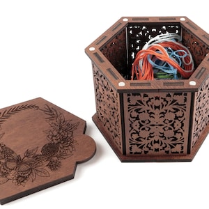 May include: A hexagonal wooden box with a floral design and a lid featuring a floral wreath with a butterfly. The box is open and filled with colorful embroidery floss.