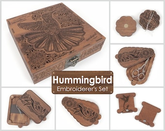 May include: Wooden embroidery set featuring a hummingbird design. The set includes a box, a needle minder, a pair of scissors, and two thread bobbins. The box is decorated with intricate carvings and the quote "Beautiful things come together one stitch at a time".