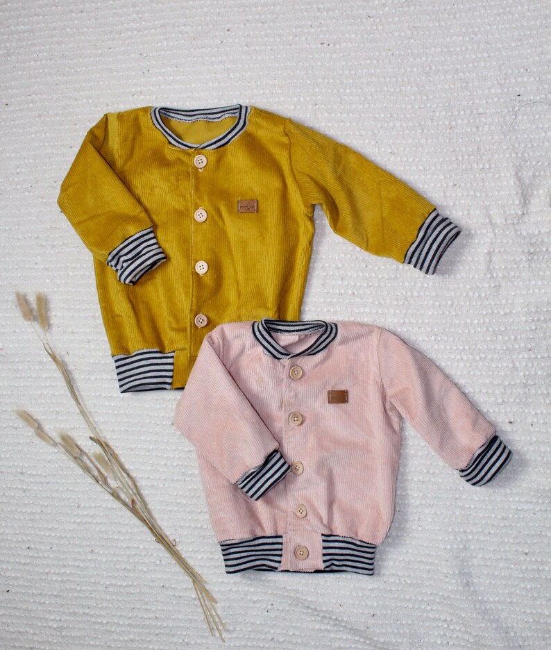 May include: Two corduroy jackets with striped cuffs. One jacket is mustard yellow and the other is light pink.