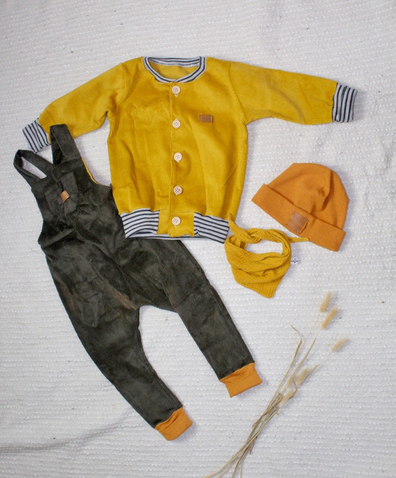 May include: A mustard yellow corduroy jacket with a white and black striped trim, a pair of dark green corduroy overalls, and a mustard yellow beanie.