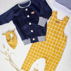 May include: A blue corduroy jacket with a white and grey striped trim, a pair of yellow checkered overalls, and a grey and white polka dot hat.