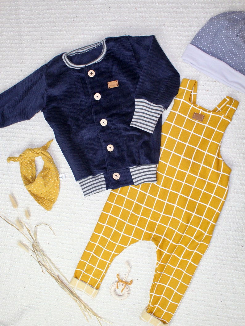 May include: A blue corduroy jacket with a white and grey striped trim, a pair of yellow checkered overalls, and a grey and white polka dot hat.