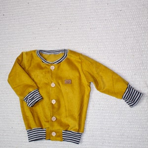 May include: A mustard yellow corduroy jacket with a button closure and black and white striped trim on the cuffs and waistband.