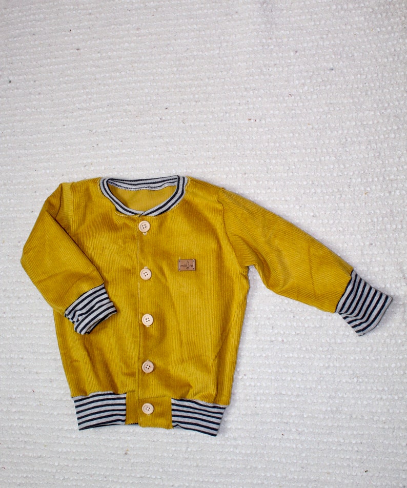 May include: A mustard yellow corduroy jacket with a button closure and black and white striped trim on the cuffs and waistband.