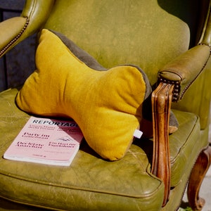 Könnte beinhalten: Ein gelbes und braunes Kissen aus Cord sitzt auf einem grünen Ledersessel. Ein rosa Magazin mit dem Titel "REPORTAGE" ist unter dem Kissen sichtbar.