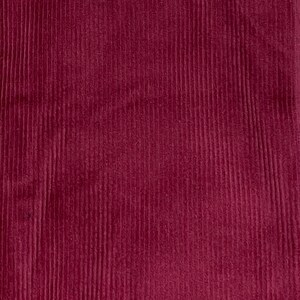 May include: A close-up of a deep burgundy corduroy fabric with a vertical ribbed texture.