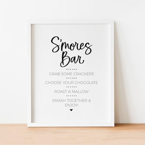 May include: A white framed sign with black text that reads "S'mores Bar" and instructions for making s'mores: "Grab some crackers, choose your chocolate, roast a marshmallow, smash together & enjoy!"