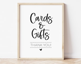 May include: A white sign with a black wooden frame. The sign says "Cards & Gifts" in black cursive lettering with "Thank You!" below it. There is a small black heart below the text.