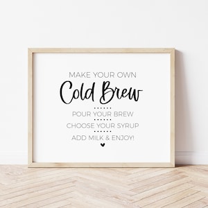 Pode incluir: Uma placa enquadrada com o texto "MAKE YOUR OWN Cold Brew POUR YOUR BREW CHOOSE YOUR SYRUP ADD MILK & ENJOY!" em texto preto sobre um fundo branco.