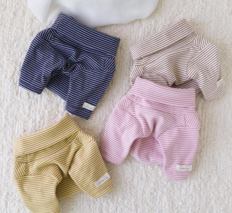 May include: Four pairs of striped dog pajamas in different colors: navy blue, beige, pink, and yellow. Each pair has a white stripe pattern and a small white tag with the word "Sunny Life" on it.