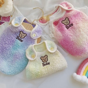 May include: Three colorful fleece dog vests with a bear and the word "Baby" embroidered on each. The vests are in shades of pink, purple, and yellow.