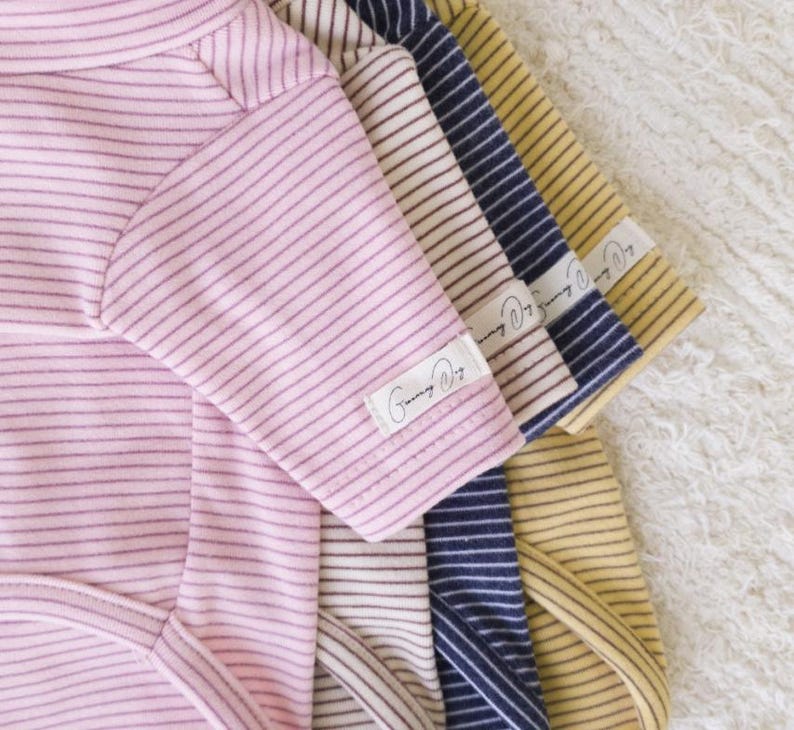 May include: Five striped baby onesies in pink, white, navy blue, yellow, and brown. The onesies have a small label that says "Sunny Days".