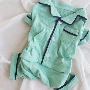 May include: A light green two-piece pajama set with black trim. The top has a collar and buttons. The shorts have an elastic waistband.