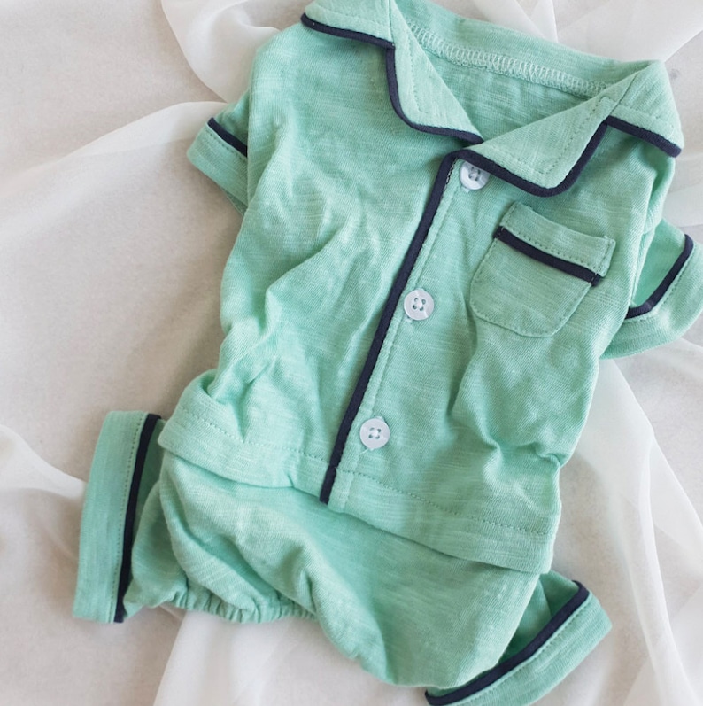May include: A light green two-piece pajama set with black trim. The top has a collar and buttons. The shorts have an elastic waistband.