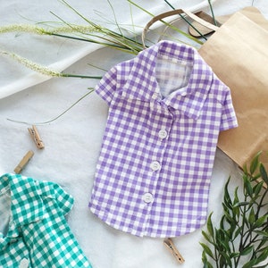 May include: A purple and white gingham button-up shirt with short sleeves. The shirt has a collar and is made of a soft, comfortable fabric.