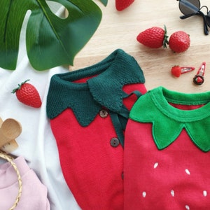 Pode incluir: Dois conjuntos de malha vermelha em forma de morango para beb&ecirc;s. Um tem uma gola verde e o outro um design de folha verde.