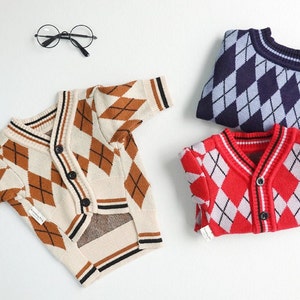 May include: Three argyle patterned cardigans in different colors: beige with brown, red with white, and navy blue with light blue. Each cardigan has a button closure and a contrasting trim.