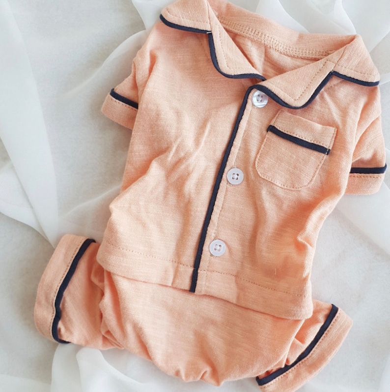 May include: A peach-colored pajama set with black trim. The top has a collar and buttons. The pants have a wide leg.