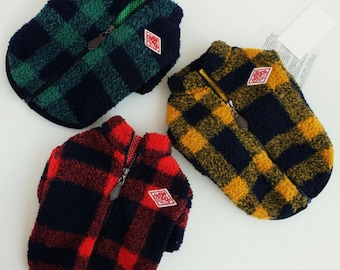 Puede incluir: Tres jerséis para perros en diferentes patrones de cuadros: verde y negro, amarillo y negro, y rojo y negro. Cada jersey tiene una cremallera y un pequeño parche en forma de diamante con el texto "GUNDOG" en rojo.