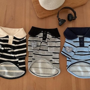 May include: Three dog shirts with striped patterns and polo collars. One shirt is black and white, another is gray and black, and the third is light blue and navy. Each shirt has a "Bigger Heart" patch.