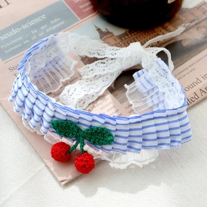 May include: A blue and white striped headband with a white lace trim and a crocheted cherry embellishment.