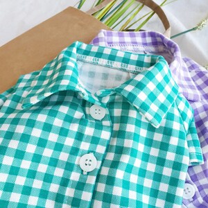 May include: A green and white gingham button-down shirt with a collar. The shirt has two buttons on the front.