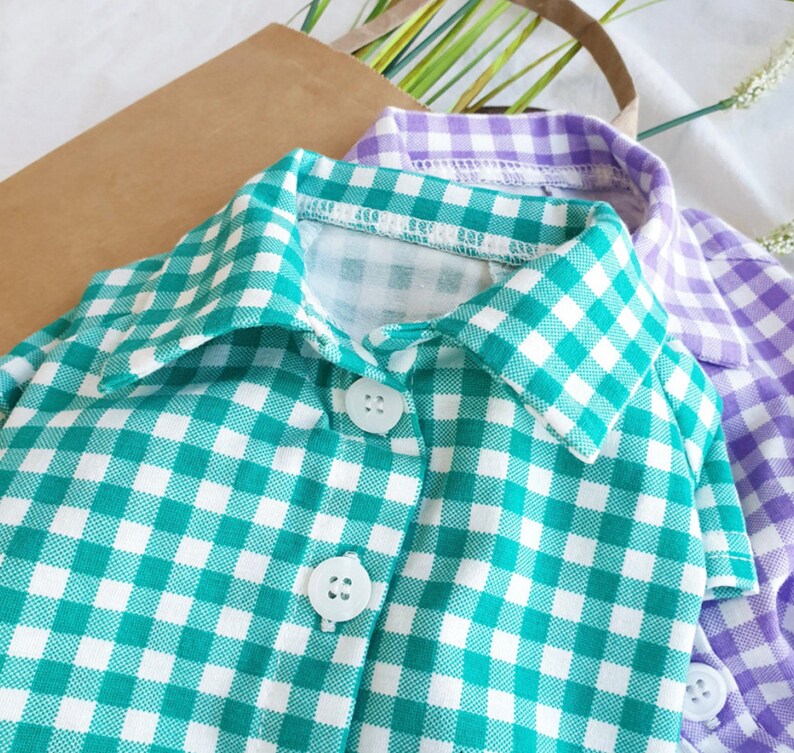 May include: A green and white gingham button-down shirt with a collar. The shirt has two buttons on the front.