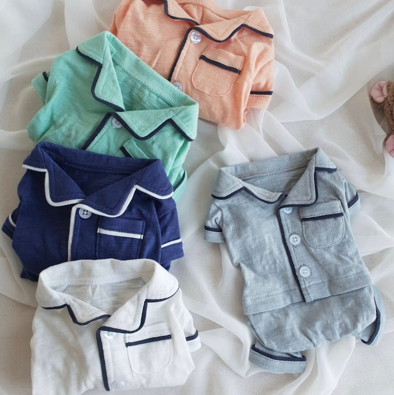 May include: Five different colored short-sleeved shirts with a collared neckline and a single button closure. Each shirt has a contrasting trim around the collar and pocket.