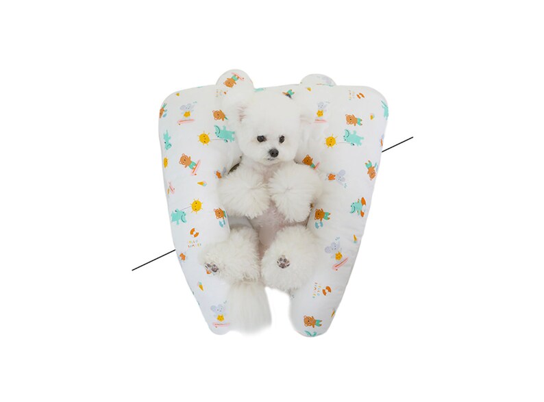 May include: A white dog with a fluffy tail is sitting in a white and green patterned dog bed. The bed is shaped like a U and has a raised edge. The dog is looking at the camera.