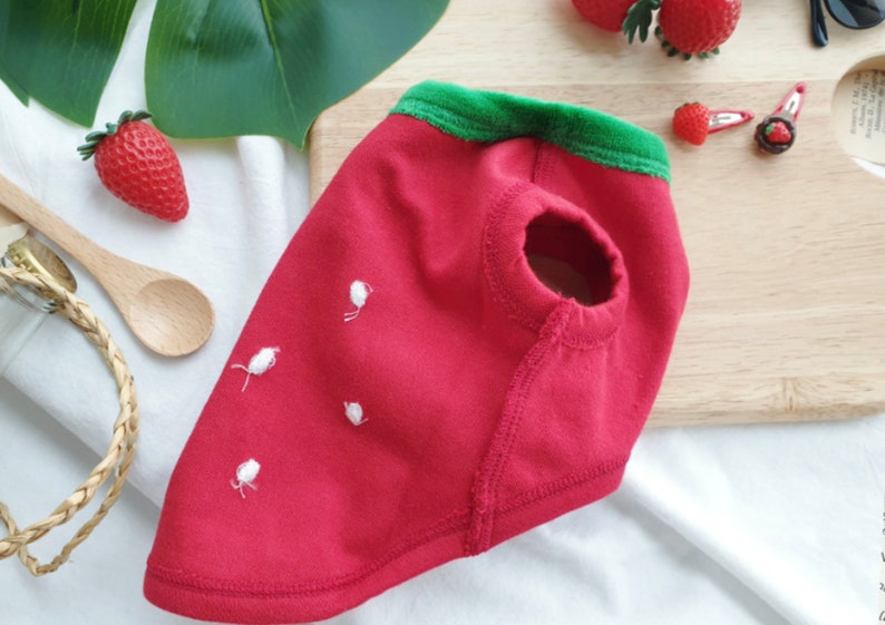 Pode incluir: Camisola de c&atilde;o vermelha de algod&atilde;o com colarinho verde e detalhes bordados brancos que se assemelham a um morango.