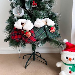 Könnte beinhalten: Ein Weihnachtsbaum, geschmückt mit Ornamenten und Haustier-Umhängen. Die Umhänge sind rot und grün kariert mit weißen Kunstfellkragen und kleinen Rentier-Ornamenten. Im Vordergrund ein Schneemann mit Weihnachtsmütze.