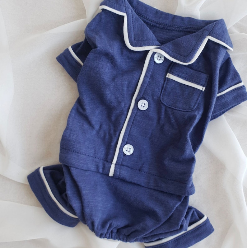 May include: A navy blue pajama set with white piping. The top has a button-up front and a pocket on the chest. The bottom is a pair of shorts.