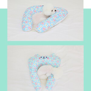 May include: A light blue and white patterned dog bed shaped like a horseshoe with a small white dog sleeping inside.