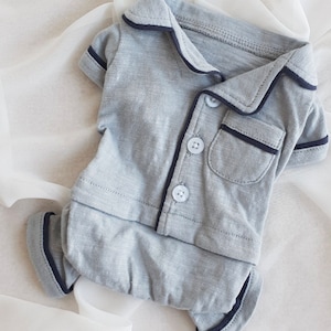 May include: A gray and navy blue baby onesie with a collared shirt top and long pants. The onesie has a pocket on the front and three buttons.