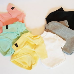 Peut inclure: Six chemises pour chien de différentes couleurs, dont rose, vert clair, jaune, blanc, gris et noir. Les chemises sont toutes à manches courtes et ont un col rond.