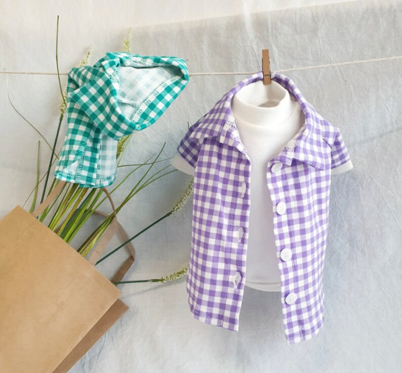 May include: Two checkered shirts, one green and one purple, hanging on a clothesline. The shirts are both short-sleeved and have a button-up front.
