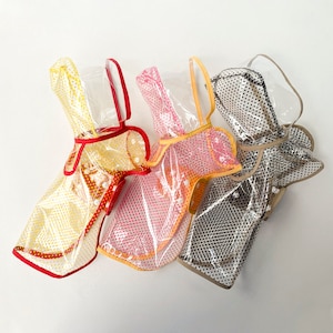 Op de afbeelding: Vier doorzichtige regenjassen met capuchon, elk met een ander stippenpatroon. De regenjassen hebben gekleurde randen in rood, oranje en bruin. De capuchons hebben een doorzichtig plastic vizier en een handvat.