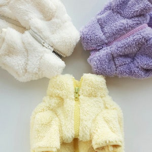 May include: Three plush jackets in different colors: white, yellow, and purple. Each jacket has a zipper down the front.