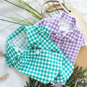 May include: Two plaid shirts for pets, one green and one purple. The shirts have a classic button-down style with a collar.