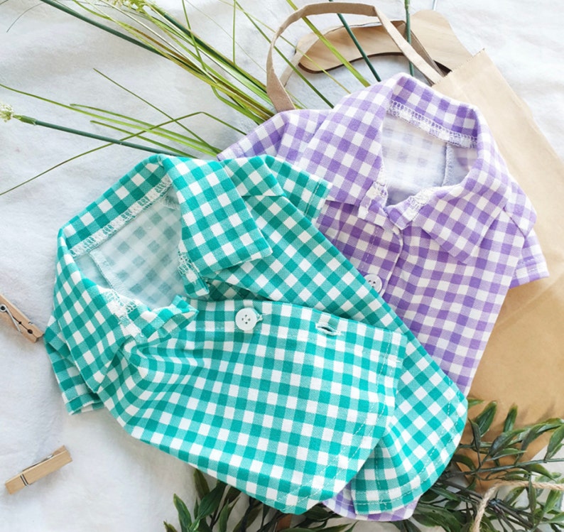 May include: Two plaid shirts for pets, one green and one purple. The shirts have a classic button-down style with a collar.