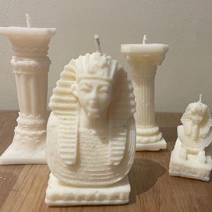 Op de afbeelding: Vier witte kaarsen, twee met traditionele ontwerpen en twee met Egyptisch geïnspireerde ontwerpen. De Egyptische kaarsen hebben een farao's hoofd en een sfinx.