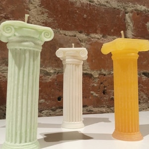 May include: Three decorative pillar candles, each with a different colour and design. The candle on the left is green and has a fluted design. The candle in the middle is white and has a smooth design. The candle on the right is yellow and has a fluted design.
