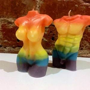 May include: Two rainbow-colored torso candles. One candle is a female form, the other a male form. The candles are in a gradient of colors, including orange, yellow, green, blue, and purple. Each candle has a wick at the top.