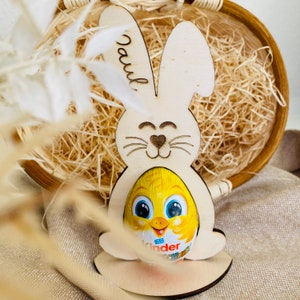 Puede incluir: Corte de conejo de Pascua de madera con el nombre "Paul" grabado en el lateral. El conejo sostiene un huevo de chocolate amarillo con un dise&ntilde;o de pollito.